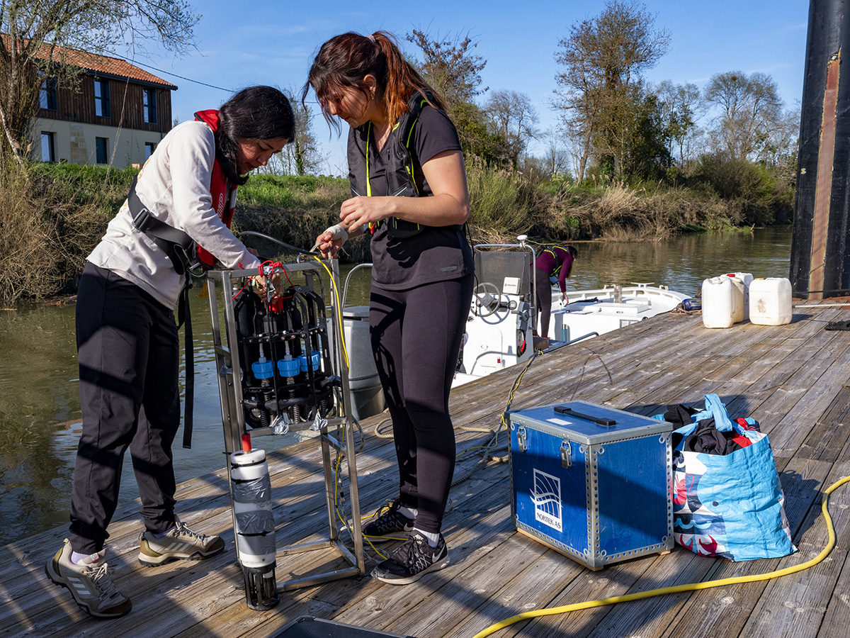 Two researchers stand on a dock fixing the Ascension depth sampler to a metal housing.