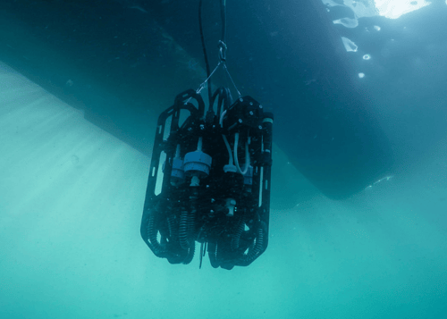 Ascension eDNA sampler is lowered into the ocean, viewed from below the instrument looking up with the shadow a boat behind the instrument.