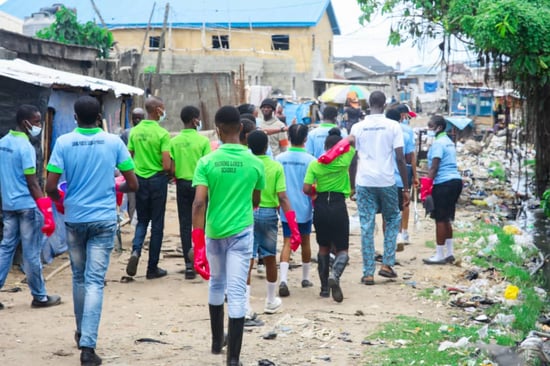 A group of Nigerian youth walk on a pathway wearing rubber gloves to complete a plastic cleanup