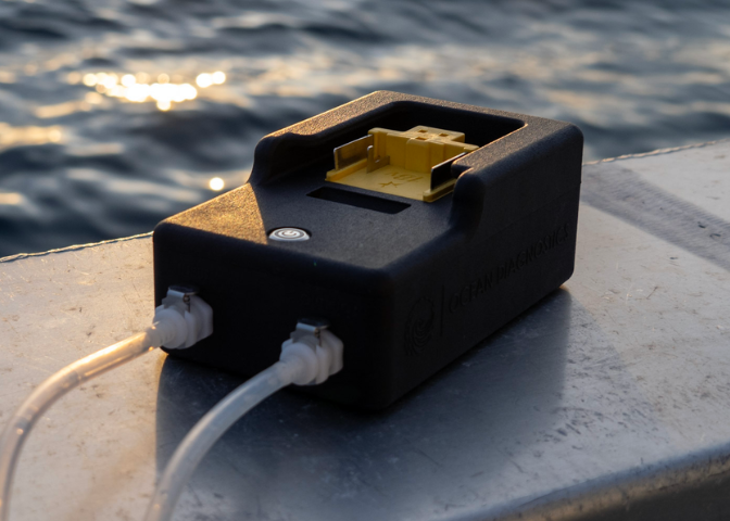 eDNA surface samplers sits on the side of a boat overlooking a setting sun on the ocean