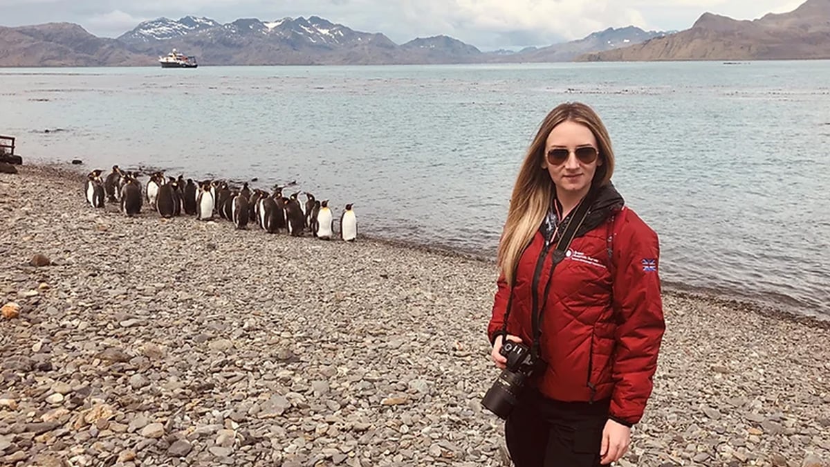 A woman researcher stands along an Antarctic shoreline beside a group of penguins