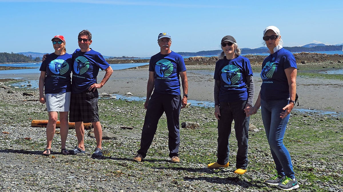 A group of five community scientists stand on the shoreline smiling at the camera