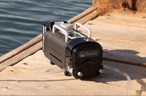 Up close view of the Discovery eDNA surface sampler pro sitting on a wooden dock with water in the background.