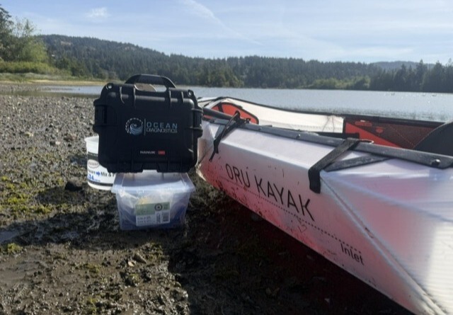 Carrying case for the eDNA Surface Sampler sits side a kayak along a rocky coastline