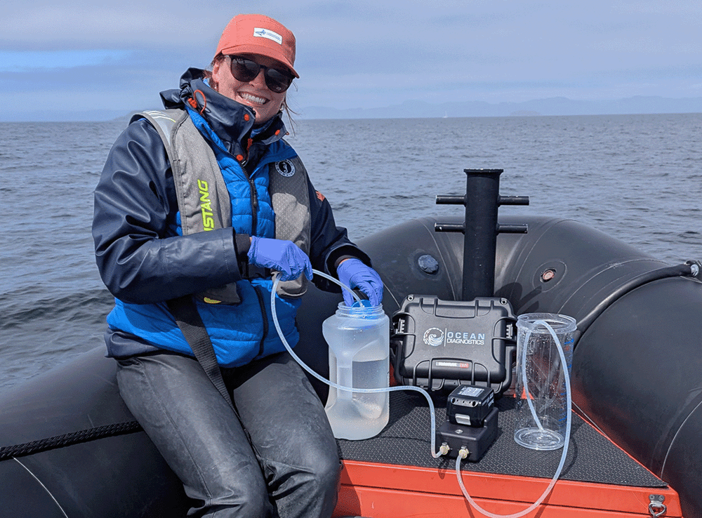 Researchers sits smiling on a small dinghy filtering water through the eDNA surface sampler
