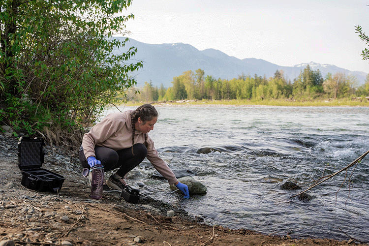 Woman kneels at the bank of a river using Ocean Diagnostics' surface sampler to collect eDNA