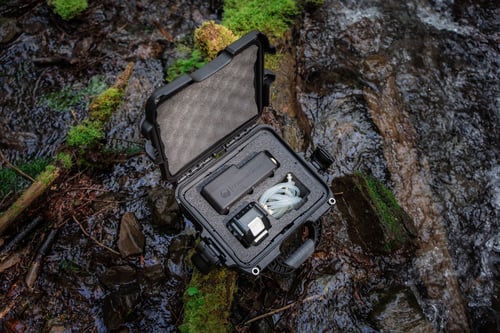 Discover eDNA surface sampler sits in an open, black and rugged carrying case in a forest stream